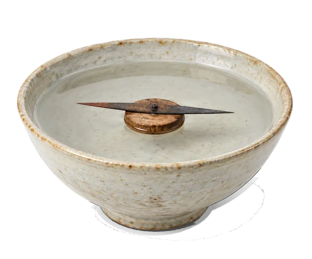 4K transparent cutout of product photography of a single ancient floating needle compass, featuring a magnetized iron needle resting on a small piece of wood floating in a simple ceramic bowl of water, is…