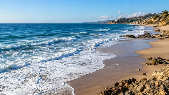 4K 16:9 photoreal photograph of a vast expanse of open ocean meeting the sandy coastline under bright coastal daylight, showcasing a real beach and coast scene.